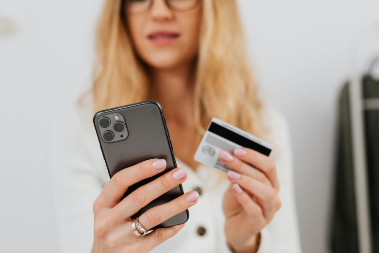 Frau mit Krankenkassenkarte in der einen und Handy in der anderen Hand.